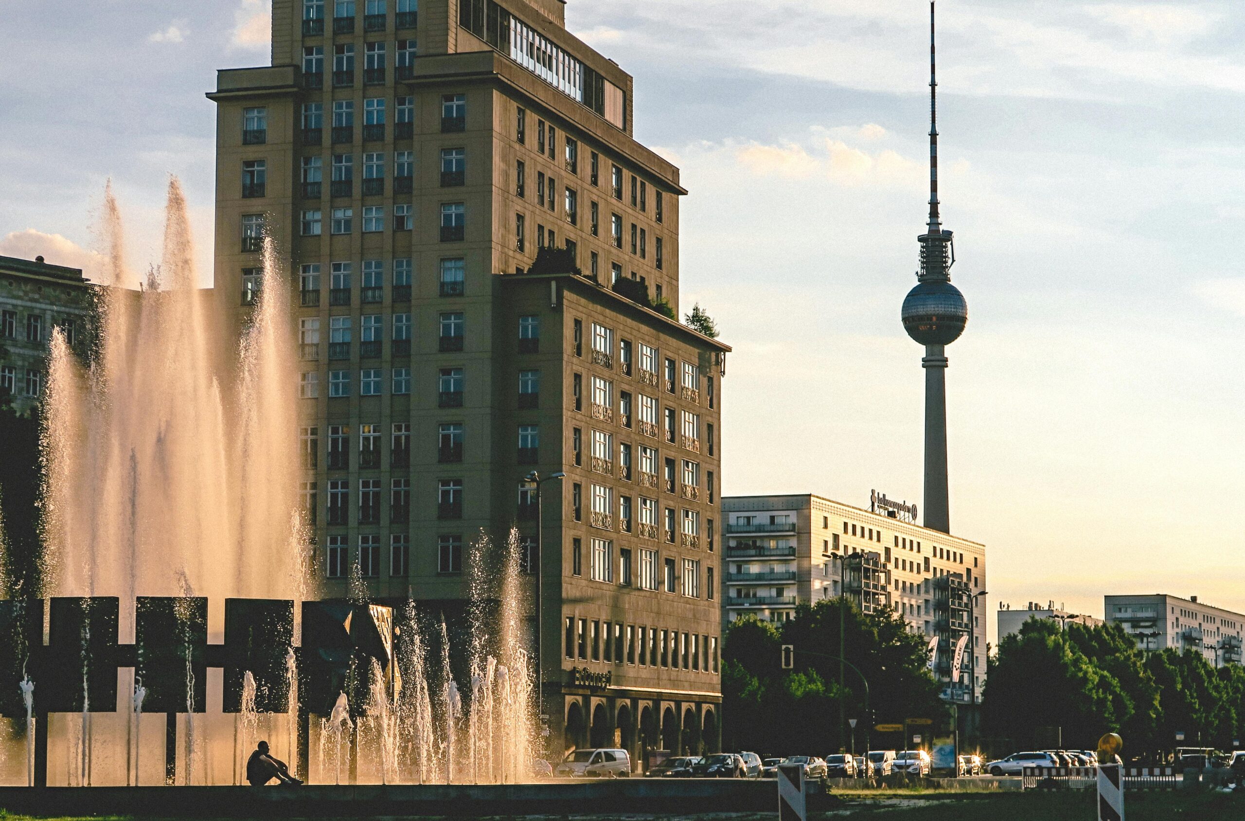 Evening view of Berlin's iconic TV Tower, modern buildings, and a lively fountain.